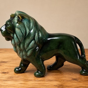 May include: A ceramic lion figurine standing in profile, featuring a glossy, deep emerald green glaze with lighter teal highlights on the mane. The sculpture depicts the animal with a textured, flowing mane and a smooth, solid-colored body.