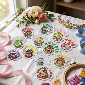May include: A collection of embroidered patches featuring Nintendo characters including Mario, Luigi, Peach, Yoshi, Rosalina, Bowser, Toad, Waluigi, Wario, Dry Bones, Daisy, and Donkey Kong, each with their name arched above or below the character.