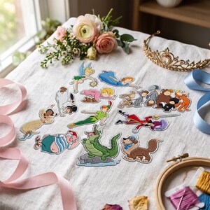 May include: A collection of embroidered patches featuring various cartoon characters including a fairy, a boy in green, a crocodile, a pirate, and a dog. The patches are arranged on a white fabric surface alongside a gold tiara and flowers.