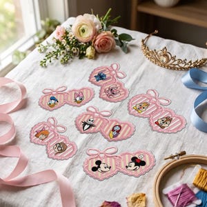 May include: A collection of heart-shaped paper cutouts featuring various cartoon characters, including Mickey and Minnie Mouse, Donald and Daisy Duck, Stitch, Angel, Chip and Dale, Jack and Sally, and others, all set against a pink striped background.