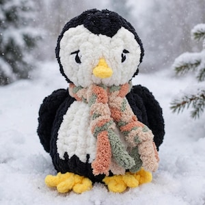 May include: A plush penguin toy crafted from black and white yarn, featuring a yellow beak and feet. The penguin wears a textured, multi-colored scarf in shades of muted orange, green, and cream, with embroidered black eyes and a soft, fuzzy finish.