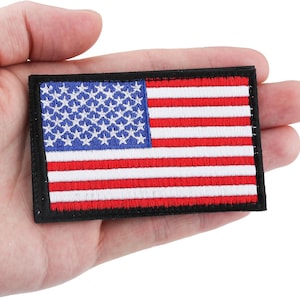 May include: A rectangular embroidered patch featuring the United States flag with a blue canton containing white stars and alternating red and white horizontal stripes, all bordered by a thick black stitched edge on a fabric base.
