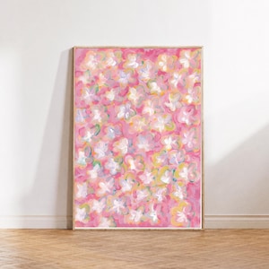 Op de afbeelding: Een rechthoekig ingelijst schilderij met een abstract bloemenpatroon in tinten felroze, zacht wit en lichtgeel. Het kunstwerk toont gelaagde, losse penseelstreken die een dicht veld van bloemachtige vormen over het canvas creëren.