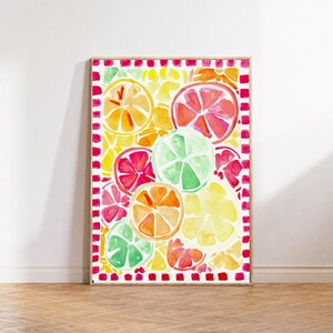 Op de afbeelding: Een rechthoekige ingelijste wandkunstprint met een aquarelillustratie van diverse gesneden citrusvruchten, waaronder sinaasappels, grapefruits, citroenen en limoenen in tinten geel, oranje, roze en groen, omrand door een rood-wit geblokt patroon.