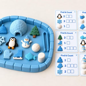 May include: A blue plastic tray with raised edges containing small winter-themed figurines including an igloo, penguin, snowman, tree, snowflake, mug, mitten, skate, fish, and ball. Six white Find & Count cards with blue text are included.