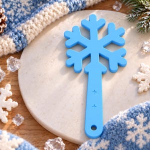 May include: A bright blue plastic snowflake-shaped tool with a long handle featuring two small star-shaped cutouts and a circular hole at the base. The snowflake design has six symmetrical arms with rounded ends, creating a distinct winter-themed shape.