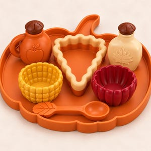 Puede incluir: Una bandeja naranja con forma de calabaza que contiene un juego de comida de juguete, incluyendo una botella naranja con una manzana, una botella beige con una hoja de arce, un cuenco amarillo, un cuenco rojo estriado, un trozo de tarta y una cuchara.