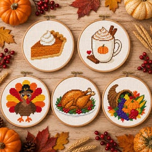 Könnte beinhalten: Fünf runde Holzstickrahmen mit Kreuzstichmotiven zum Thema Thanksgiving: ein Stück Kürbiskuchen, eine Tasse gewürzter Latte, ein Truthahn, ein gebratenes Huhn auf einer Platte und ein Füllhorn gefüllt mit herbstlichen Ernteprodukten.