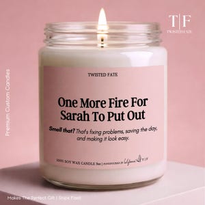 May include: A clear glass jar candle with white soy wax and a lit wick. The label is light pink with black text reading: TWISTED FATE, One More Fire For Sarah To Put Out, Smell that? That's fixing problems, saving the day, and making it look easy.