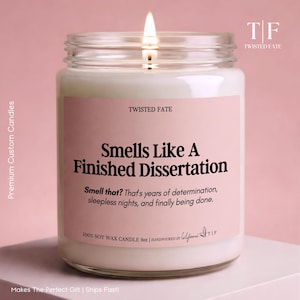 May include: A 9oz soy wax candle in a clear glass jar with a lit wick. The pink label features the text: Twisted Fate, Smells Like A Finished Dissertation, Smell that? That's years of determination, sleepless nights, and finally being done.