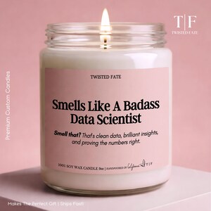 May include: A 9oz soy wax candle in a clear glass jar with a lit wick. The pink label features the text: TWISTED FATE, Smells Like A Badass Data Scientist, Smell that? That's clean data, brilliant insights, and proving the numbers right.