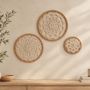 Könnte beinhalten: Drei kreisförmige Wandbehänge mit cremefarbenen Häkeldeckchen in beigefarben umwickelten Reifen. Die Designs zeigen komplizierte, symmetrische Muster mit durchbrochenen Maschen und variieren in ihrer Größe von groß bis klein.