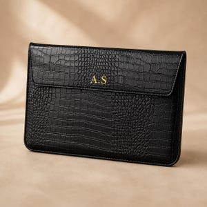 May include: A black rectangular laptop sleeve featuring a textured crocodile skin pattern. The front flap is embossed with the gold-colored initials A.S. centered in the middle. The sleeve has a structured design with clean, stitched edges.