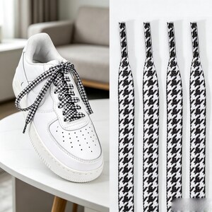 May include: A white sneaker with a perforated toe box and a thick rubber sole, featuring black and white houndstooth patterned shoelaces. Four individual black and white houndstooth patterned shoelaces are displayed vertically next to the sneaker.