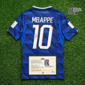 Puede incluir: Una camiseta de fútbol azul con el nombre MBAPPE y el número 10 en blanco con borde dorado en la parte posterior. La camiseta incluye una firma negra sobre el número y un certificado de autenticidad rectangular con texto, más un logo ZKICKEM.