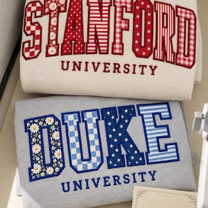 Könnte beinhalten: Ein cremefarbenes Sweatshirt mit STANFORD UNIVERSITY in rot gemusterten Buchstaben und ein graues Sweatshirt mit DUKE UNIVERSITY in blau gemusterten Buchstaben. Eine quadratische Karte mit dem Text Thank You und einem Herz ist unten rechts.