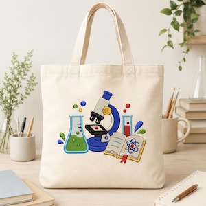 May include: A cream-colored canvas tote bag featuring an embroidered science-themed design. The graphic includes a blue microscope, a green liquid-filled Erlenmeyer flask, a red liquid-filled test tube, and an open book with an atom illustration.