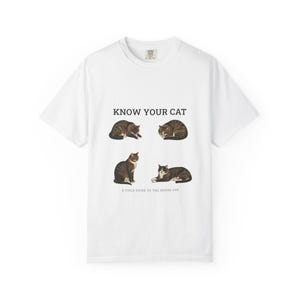 Może przedstawiać: Biały t-shirt z krótkim rękawem z nadrukiem graficznym przedstawiającym cztery brązowo-czarne koty pręgowane w różnych pozach. Tekst nad kotami brzmi "KNOW YOUR CAT", a tekst poniżej "A FIELD GUIDE TO THE HOUSE CAT" czarnymi literami.