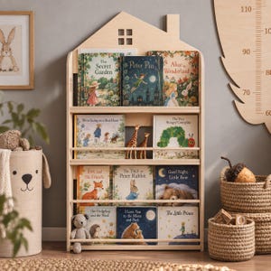 Könnte beinhalten: Ein helles, hausförmiges Bücherregal aus Holz mit drei Regalebenen. Die Regale sind mit verschiedenen Kinderbüchern gefüllt, darunter Titel wie The Secret Garden, Peter Pan, Alice in Wonderland und The Little Prince.