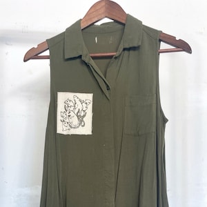 May include: A sleeveless green button-down shirt dress with a white patch featuring a graphic of several cats.