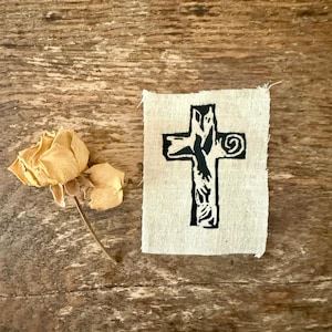 May include: A black cross with a floral design is printed on a beige fabric patch.