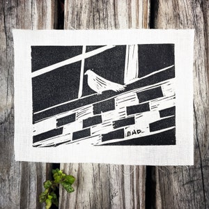 May include: Black and white linocut print of a bird perched on a brick wall. The print is signed "BAB" in the lower right corner.