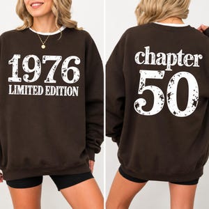 May include: A dark brown crewneck sweatshirt featuring white distressed text. The front displays 1976 LIMITED EDITION, while the back features the text chapter 50. The garment has long sleeves and a ribbed collar, showcasing a graphic design.
