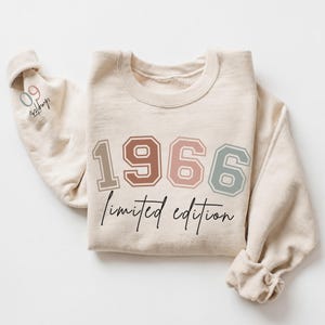May include: A beige crewneck sweatshirt featuring the year 1966 in large, multi-colored block numbers across the chest. Below the numbers, the text "limited edition" is printed in black script. The sleeve displays the text "09 chapter" in black.