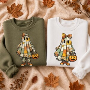 May include: An olive green sweatshirt and a white sweatshirt, each featuring a graphic of a ghost wearing a patchwork quilt pattern. The ghost on the olive sweatshirt wears a beanie, while the ghost on the white sweatshirt wears a bow.