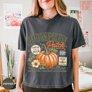 Op de afbeelding: Een antracietgrijs T-shirt met korte mouwen en een grafische print van een grote oranje pompoen met groene bladeren. De tekst luidt PUMPKIN PATCH, FRESH FROM THE PATCH, FARM FRESH, LOCALLY GROWN, PUMPKINS, CORN MAZE en APPLE CIDER.