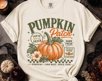 Op de afbeelding: Een ivoorkleurig t-shirt met korte mouwen en een afbeelding van een grote oranje pompoen met groene bladeren. De tekst luidt PUMPKIN Patch, FRESH FROM THE PATCH, FARM FRESH, LOCALLY GROWN, AUTUMN PICKED, PUMPKINS, CORN MAZE en APPLE CIDER.