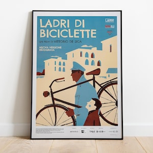 May include: A framed movie poster for Ladri di Biciclette, a film by Vittorio De Sica. The illustration features a person in a blue uniform walking with a bicycle alongside a child in a brown jacket, set against a light-colored building background.