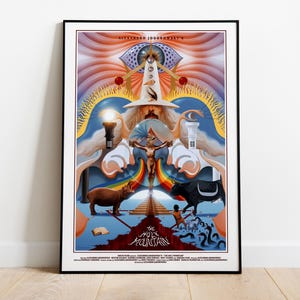 May include: A framed movie poster for Alejandro Jodorowsky's The Holy Mountain. The artwork features a central figure in a white hat, a crucified figure, a brown hippopotamus, a black bull, a pyramid, and a large eye at the top with text.