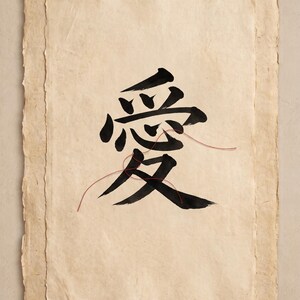 May include: A rectangular piece of textured, off-white handmade paper featuring a large black ink calligraphy character for love. A thin red thread is draped across the center of the character. A small red square seal with white text is in the corner.