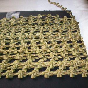 May include: Green and gold trim with a repeating bow pattern. The trim is made of a soft, woven fabric.