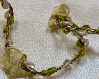 May include: Close-up of a delicate floral garland. The garland features small, pale yellow fabric roses and green and white accents. The stems are a twisted gold and brown colour, creating a vintage aesthetic.