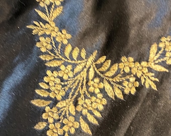 May include: Black fabric with a gold embroidered floral design. The design features a repeating pattern of leaves and flowers.