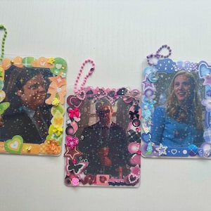 May include: Three rectangular plastic photo holders with ball chain loops. The left frame features green and orange accents with a gummy bear charm. The centre frame has pink and black decorations. The right frame displays blue and purple embellishments.