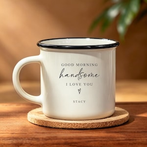 May include: A white ceramic mug with a black rim and handle, featuring the black printed text "GOOD MORNING handsome I LOVE YOU" followed by a small heart symbol and the name "STACY" centred on the front of the mug.