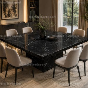 May include: A large square dining table featuring a polished black marble surface with white veining, supported by a thick central pedestal base. Eight upholstered chairs with light beige fabric seats and dark wooden legs surround the table.