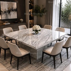 May include: A large square dining table with a polished white and grey marble top and a matching marble pedestal base. Eight upholstered dining chairs with light beige fabric seats and dark wood legs are arranged around the table. A glass vase with white flowers sits in the centre.