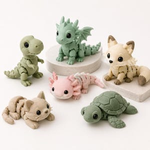 Puede incluir: Una colección de seis figuras de animales articuladas que incluye un dinosaurio verde, un dragón verde, un zorro beige, un ajolote rosa, un gato beige y una tortuga verde. Cada figura presenta un diseño de cuerpo segmentado con superficies mate y ojos negros.