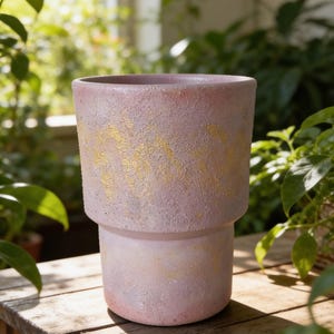 Peut inclure: Un pot de fleurs cylindrique avec une finition mate et texturée dans des tons de rose pâle et de lavande. L'extérieur présente une bande horizontale de détails en feuille d'or appliqués selon un motif irrégulier et tacheté sur la partie supérieure.