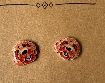 Può includere: Un paio di orecchini a bottone con un'illustrazione di un cane marrone e bianco in stile cartone animato. Gli orecchini sono su una carta marrone con il testo "Montse Designs" e "Etsy.com/shop/Montsedesigns".