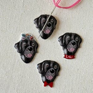 Puede incluir: Cuatro pines de cabeza de perro Labrador Retriever negro con diferentes dise&ntilde;os. Un pin tiene una corona floral, uno tiene una pajarita roja, uno tiene un collar rojo con el nombre "Loki" y uno no tiene adornos.