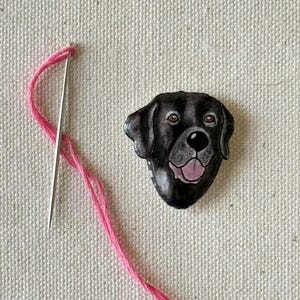 Puede incluir: Una ilustraci&oacute;n de la cabeza de un perro Labrador Retriever negro, con ojos marrones y una lengua rosa. La ilustraci&oacute;n est&aacute; sobre un fondo blanco.