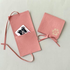 May include: Two pink felt card holders. One is open, revealing a card with a black and white dog illustration. The other is closed with a paw print and heart design. Both have a ribbon tie closure.