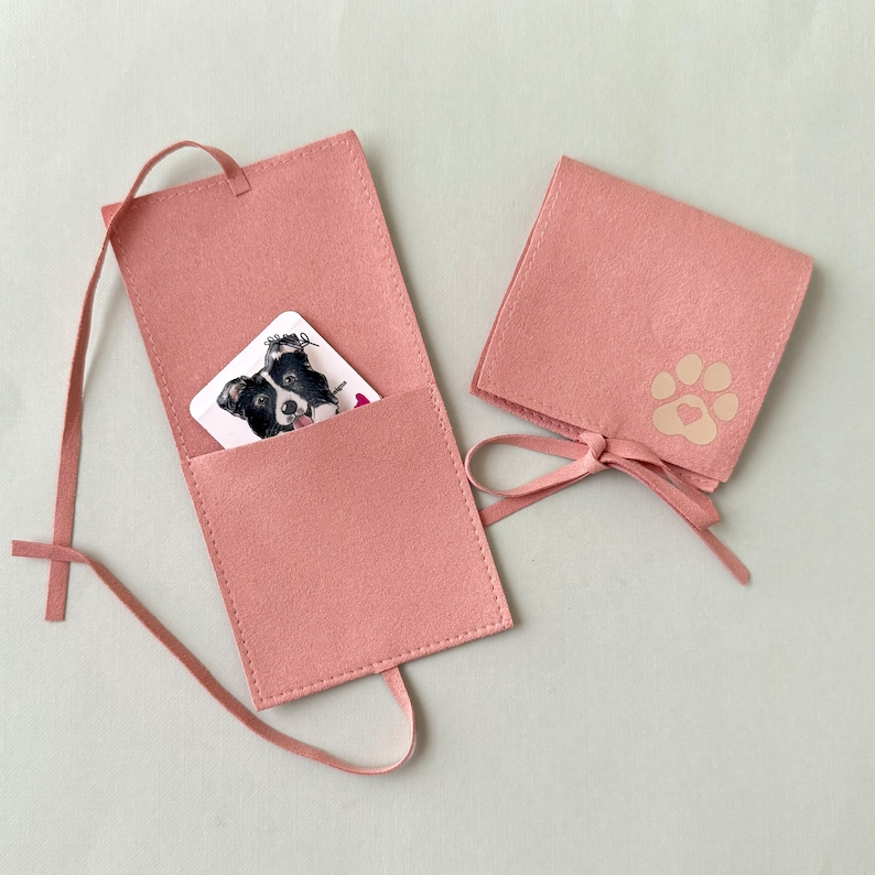 May include: Two pink felt card holders. One is open, revealing a card with a black and white dog illustration. The other is closed with a paw print and heart design. Both have a ribbon tie closure.