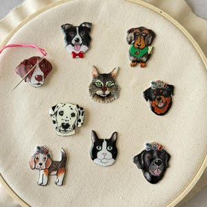 Puede incluir: Ocho pines de animales diferentes, incluyendo un d&aacute;lmata blanco y negro, un gato blanco y negro, un perro blanco y negro con una corona de flores, un labrador negro con una corona de flores, un perro marr&oacute;n y blanco con una corona de flores, un border collie blanco y negro, un dachshund marr&oacute;n y blanco y un pointer marr&oacute;n y blanco.