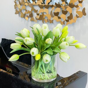 May include: A clear glass vase filled with white and yellow tulips. The vase is sitting on a black surface.